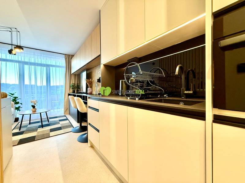 A kitchen in a studio apartment with a dining table, shelves, and a view through a large window.