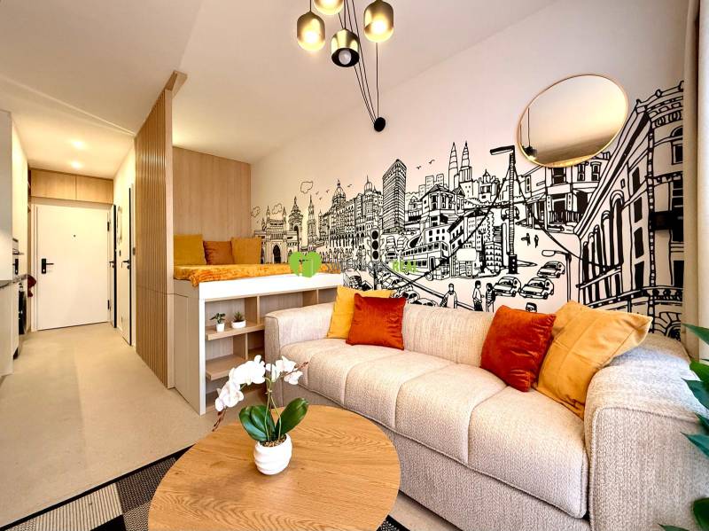 Interior of a 1-room apartment with a comfortable couch, illustrated wall, and wooden decor flooring.