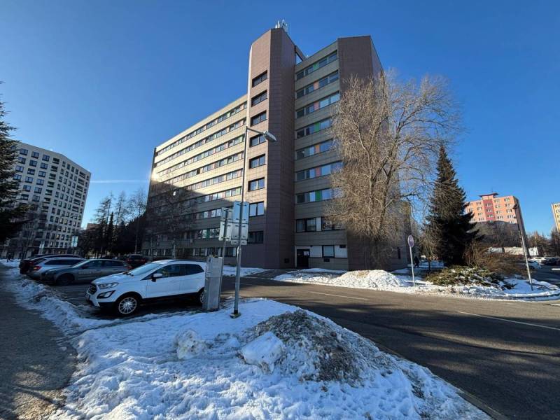 An office building in Poprad surrounded by snow and parked cars.