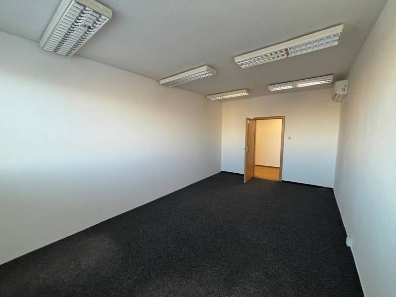 Office room with dark carpet, white walls, and ceiling lighting.