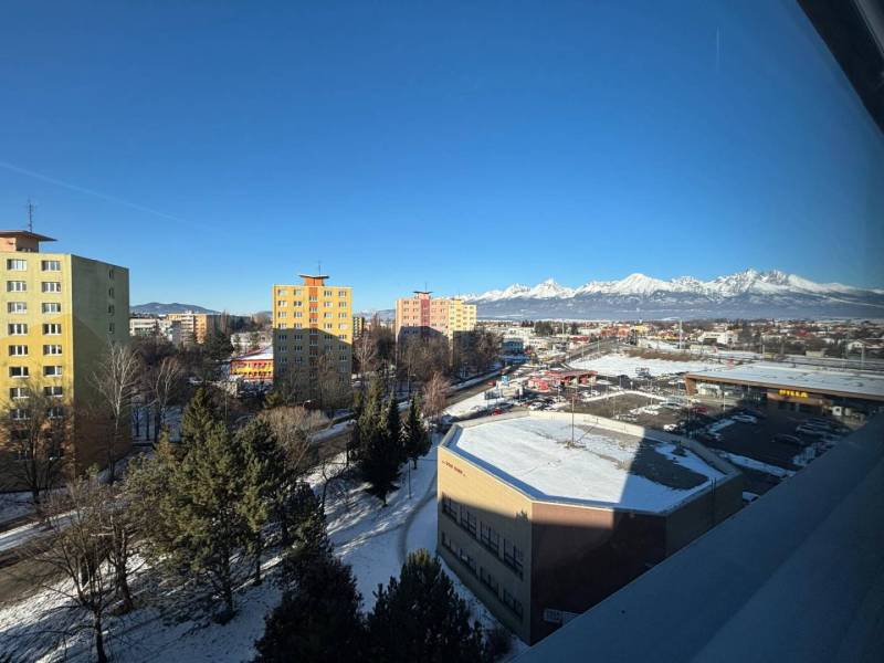 Poprad: apartment buildings, supermarkets, and snow-covered mountains behind offices under a clear sky.