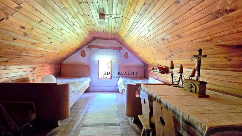 Attic room with wooden paneling, two beds, and a table in a family house.