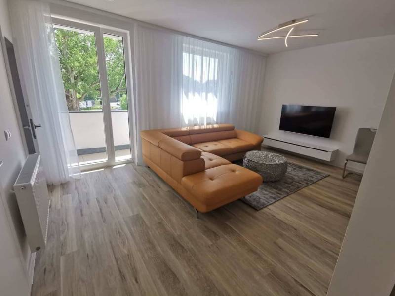 Living room in a two-room apartment with a wooden decor floor and an orange sofa.