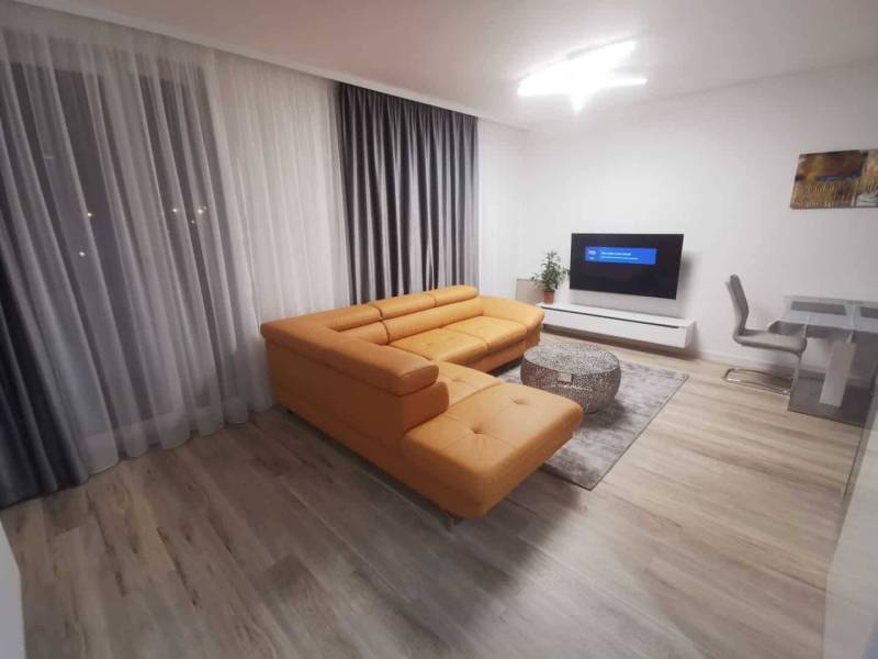 Living room in a two-room apartment with an orange sofa and a wooden decor floor.