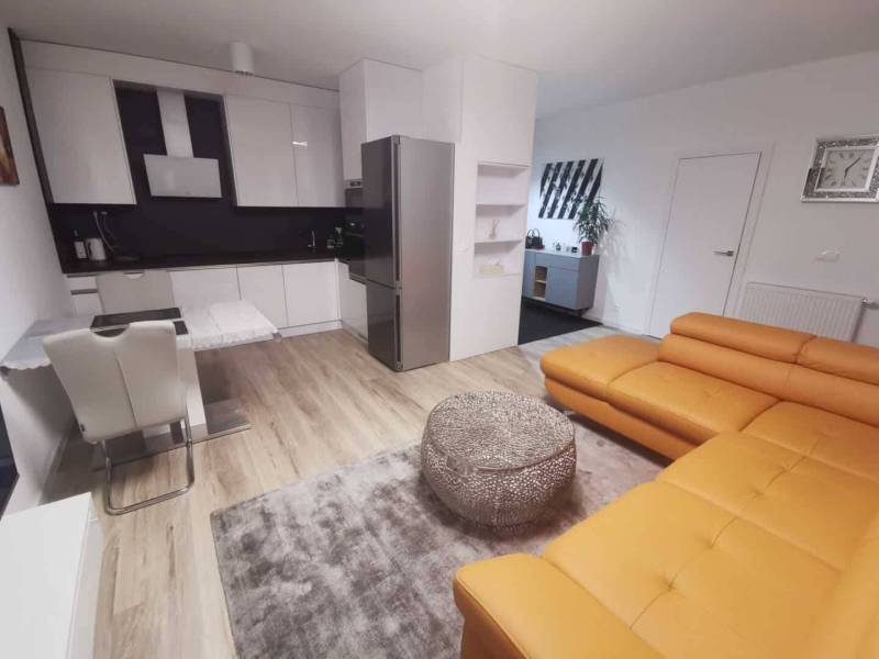 Living room connected to the kitchen in a two-room apartment, wooden decor flooring, orange sofa.