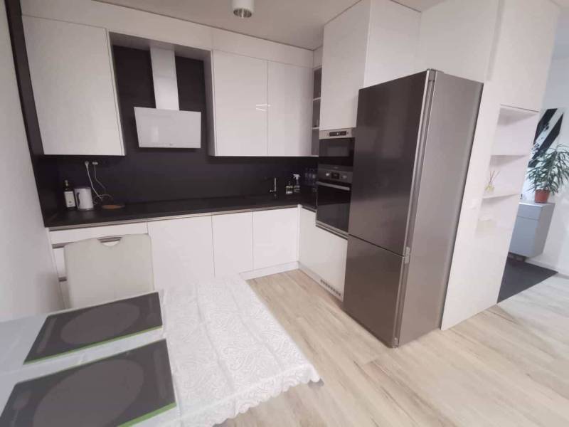 A kitchen in a 2-room apartment with white cabinets and a wooden decor floor.