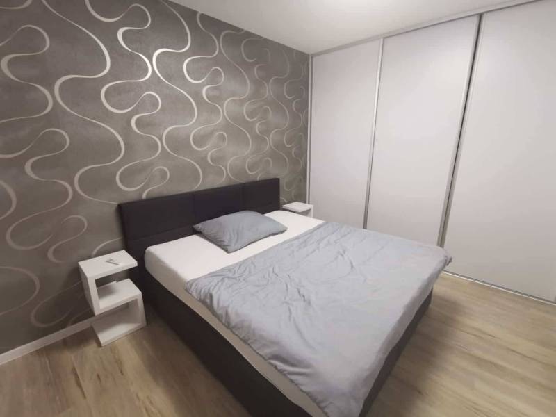 A bedroom in a two-room apartment with a wooden decor floor and wallpaper on the wall.