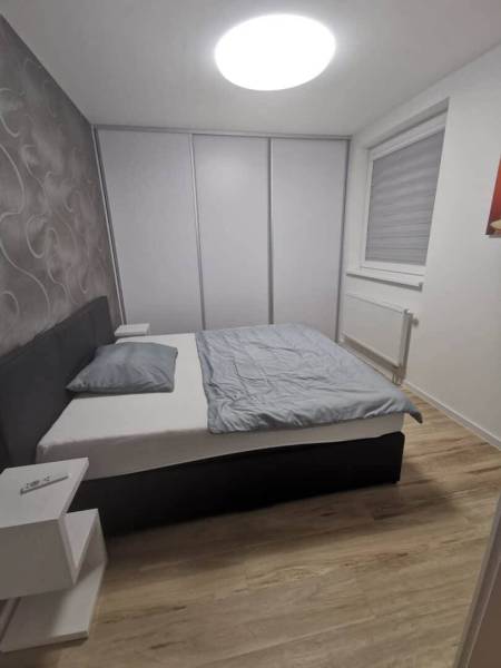 A bedroom in a two-room apartment with a wood-patterned floor and a built-in wardrobe.