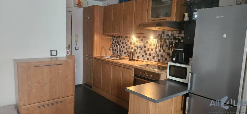 A kitchen in a studio apartment with wooden cabinets, tiled backsplash, appliances, and a white wall.