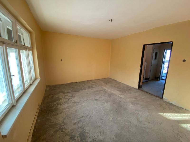 A room in a family house with a large window and bare floor, without furniture.