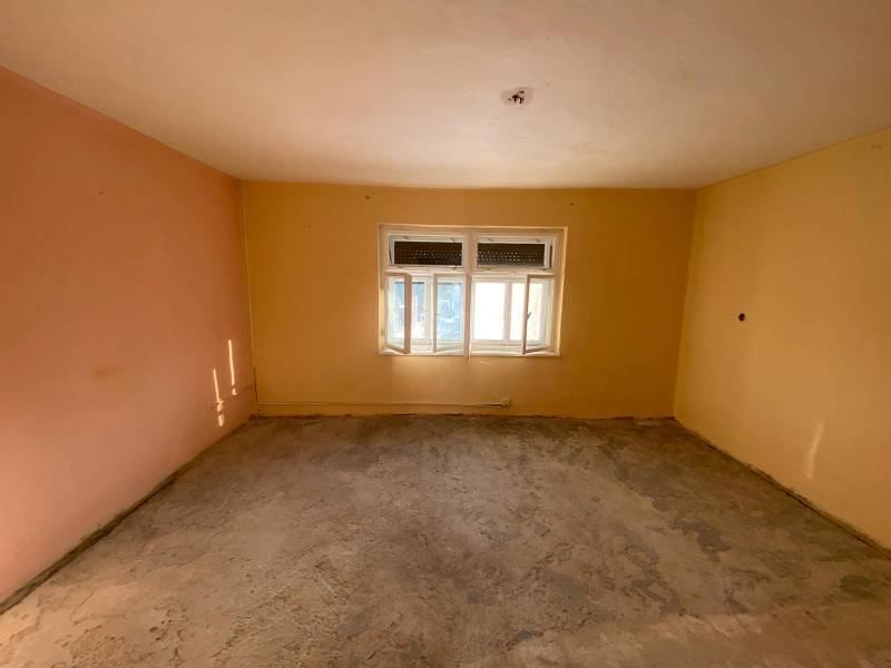 A spacious room with a window and light yellow and peach walls in a family house.