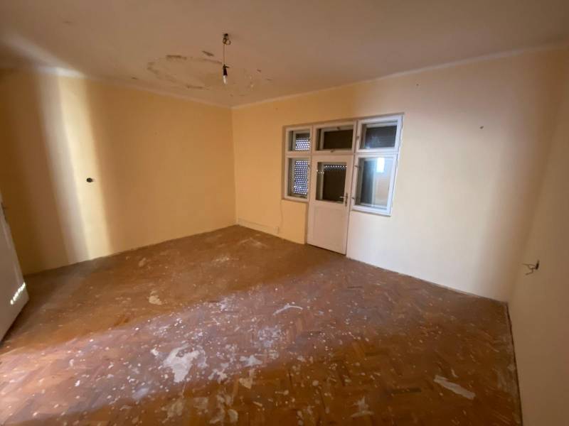 A room with windows, doors, light-colored walls, and a wooden-patterned floor in a family house.