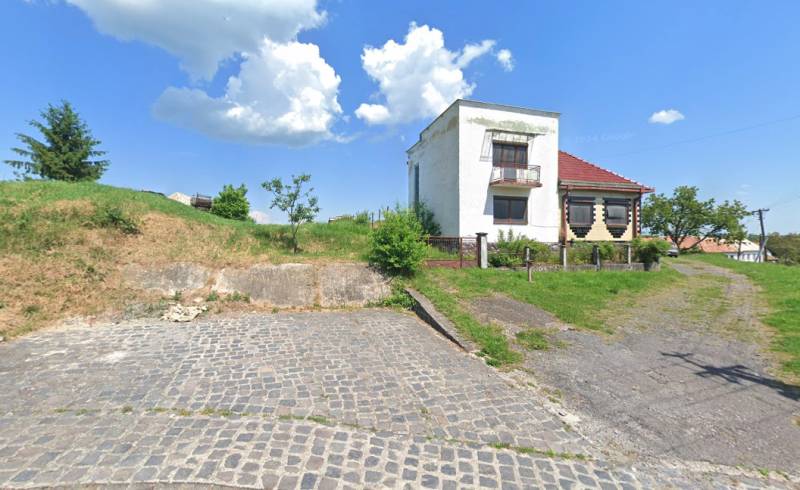 A family house in Nová Bašta surrounded by a green lawn and a paved walkway.