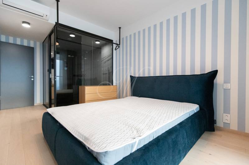 Bedroom in a 2-room apartment with a blue bed and a striped wall, floor with wood decor.