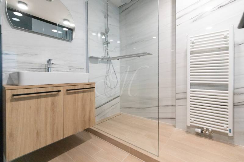 Bathroom with a sink on a wooden cabinet, a shower corner, and a floor with a wooden decor.