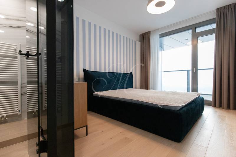 Bedroom with a large bed, wooden decor flooring, and access to a balcony in a 2-room apartment.