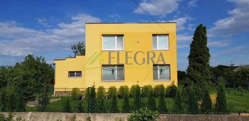 A yellow family house in Stretavka with a garden, surrounded by green bushes and a fence.