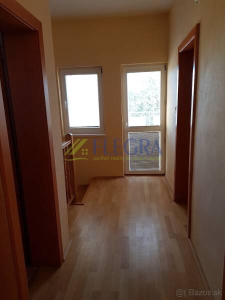 A hallway in a family house with a wood-patterned floor and windows.