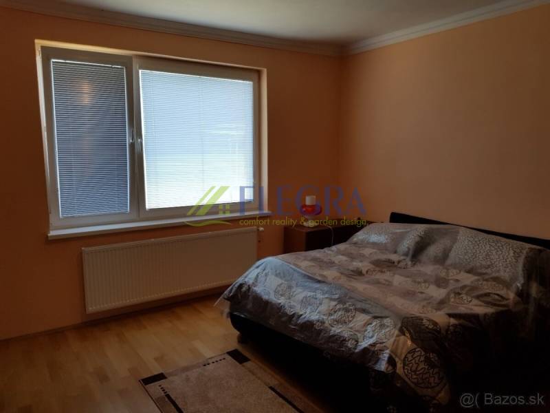 Bedroom with a window, bed, and wood-patterned floor in a family house.