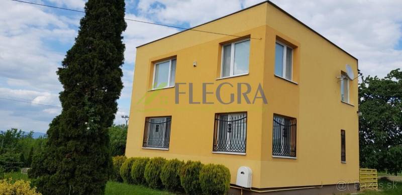 A family house in Stretavka with a striking yellow facade, surrounded by greenery and tall trees.
