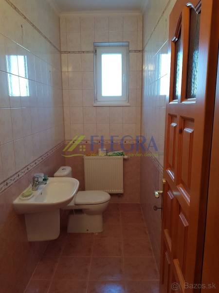 A bathroom with a sink and toilet, tiled with light tiles, in a family house.