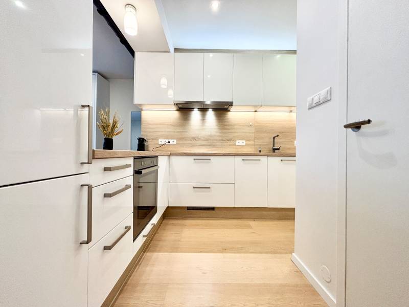 A kitchen in a 3-room apartment with white cabinets and a wooden decor floor.