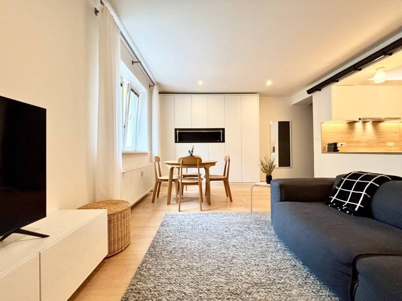 Living room with wood-patterned flooring and a kitchenette in a three-room apartment.