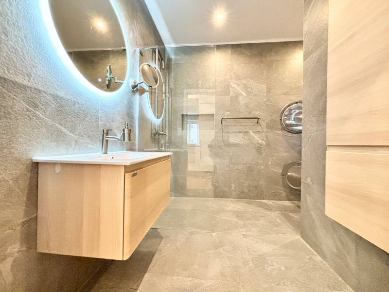Bathroom with a round mirror, shower corner, and wooden decor in a 3-room apartment.