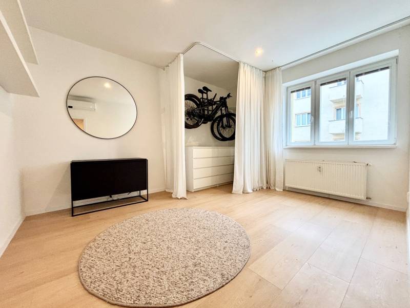 A room with a wooden decor floor, a carpet, a mirror, and a curtain in a 3-room apartment.