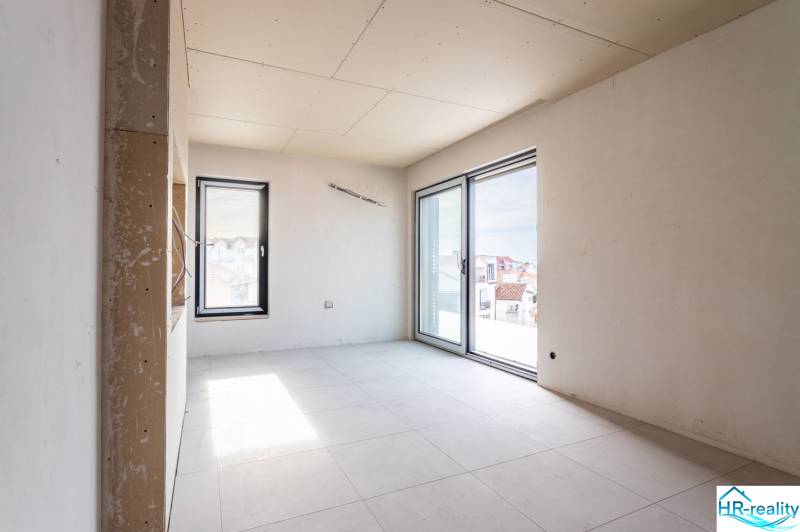 A room under construction with tiles and large windows in a 3-room apartment.