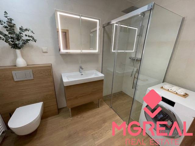 Bathroom with a shower, wooden decor flooring, and a washing machine in a 3-room apartment.