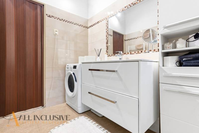 Bathroom in a family house with light tiles, a washing machine, and a mirror.