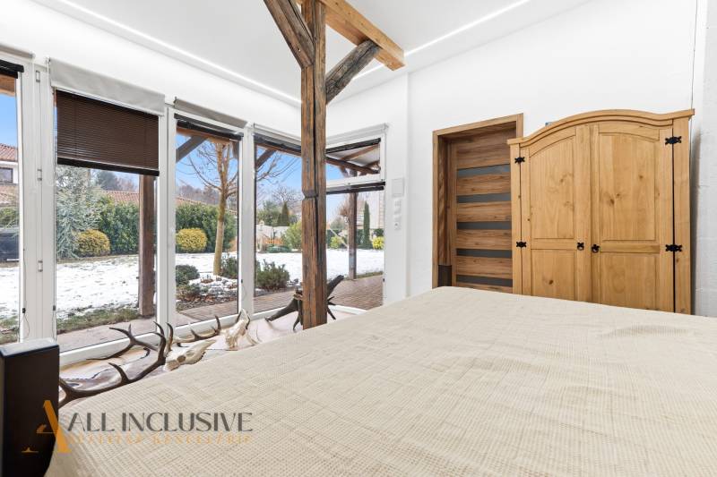 A bedroom in a family house with a view of the snowy garden, wooden decor, and massive beams.