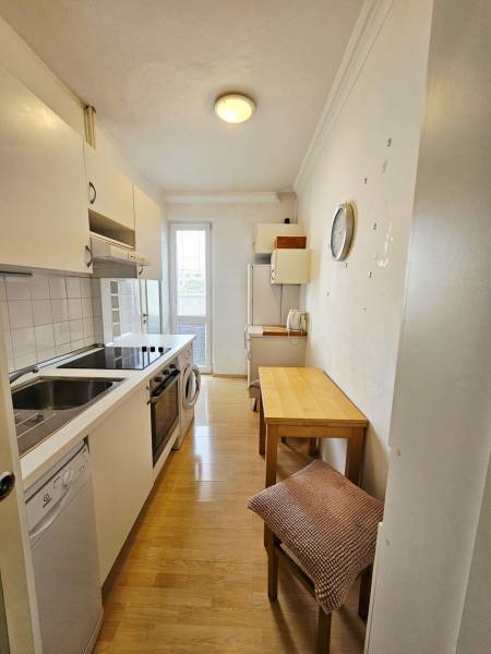 A kitchen in a 2-room apartment with appliances, a table, and a wooden decor floor.