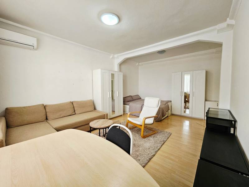 Living room in a two-room apartment with a wooden decor floor and simple furnishings.