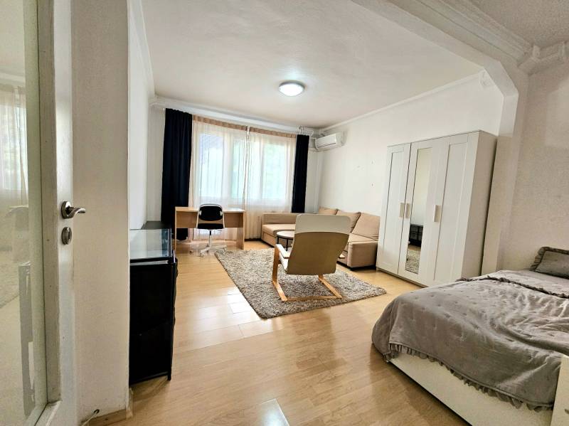 A bright living room in a two-room apartment with a wood-patterned floor and comfortable furniture.