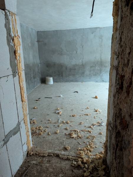 A room in a family house with a concrete floor, visible construction foam, and rough walls.