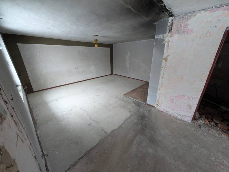Empty room with white walls in a family house. The floor is concrete with a small section of wooden decor.