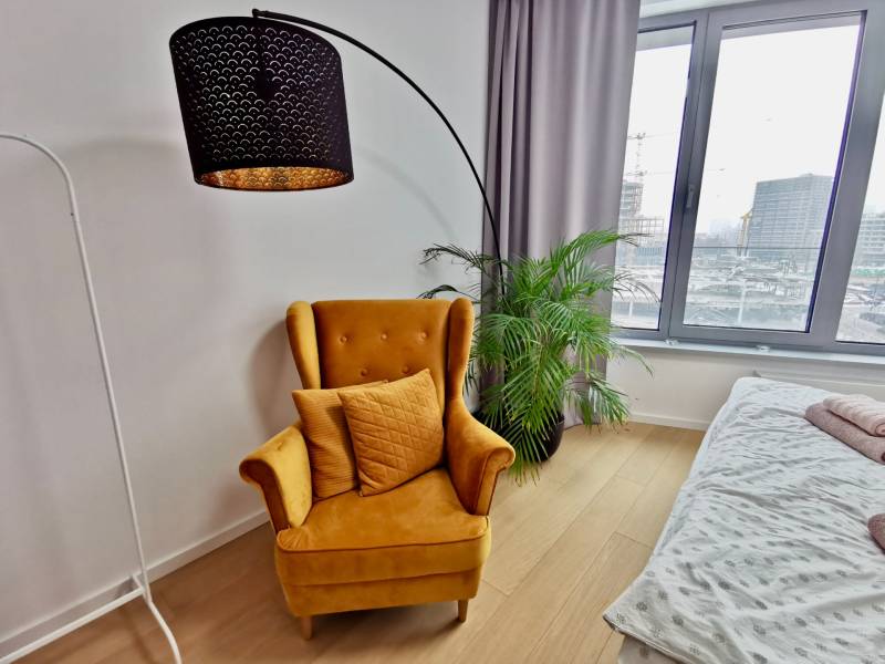 Yellow chair and houseplant in a 3-room apartment with wood-patterned flooring.