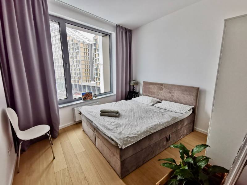 A bright bedroom in a three-room apartment with a view, a bed, and a wooden-decor floor.