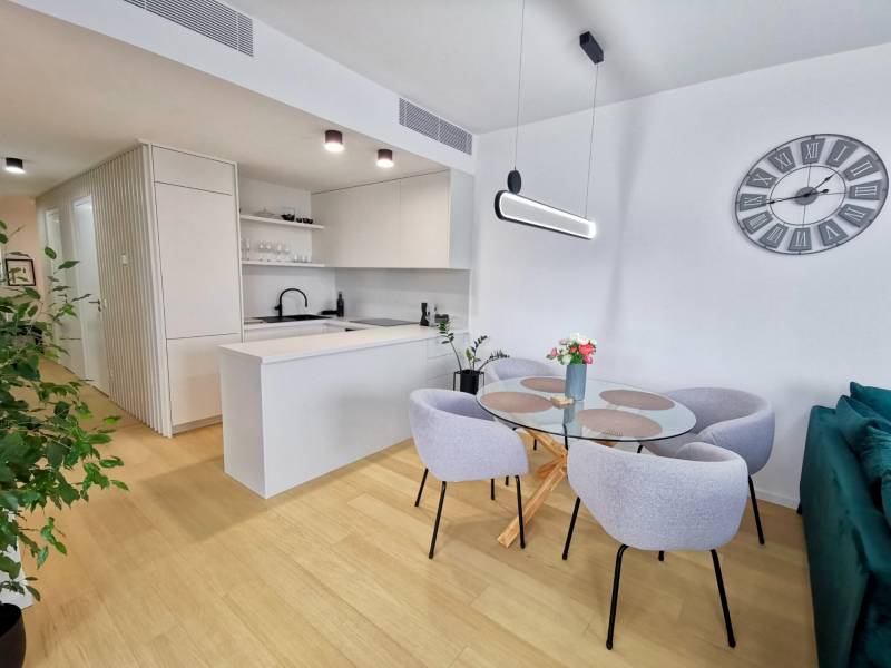 Dining table with chairs in a 3-room apartment, white walls, wooden decor flooring.