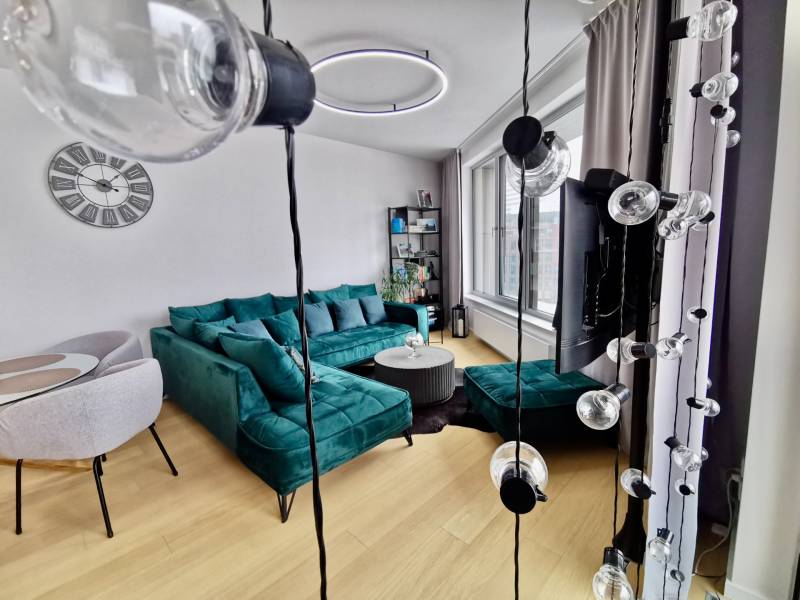 Living room in a 3-room apartment with a turquoise sofa, circular chandelier, and wooden decor flooring.
