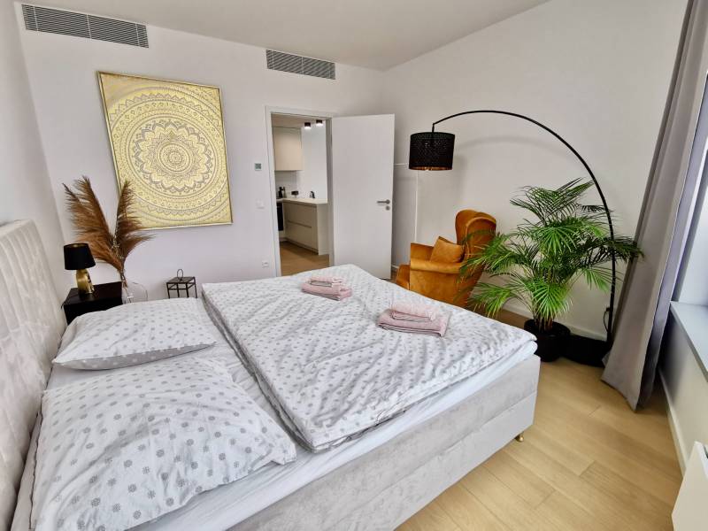 Bedroom with a double bed, plant, chair, and painting, floor with wood decor.