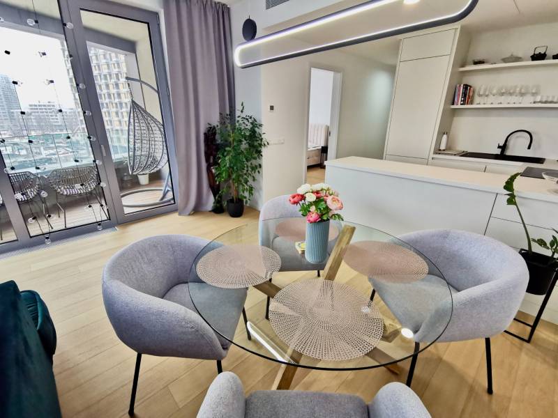 Interior of a 3-room apartment with wood-patterned flooring, a glass table, and a balcony.