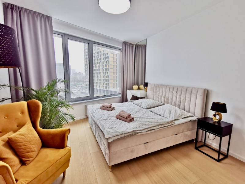 Bright bedroom in a 3-room apartment with large windows, a bed, and a chair.