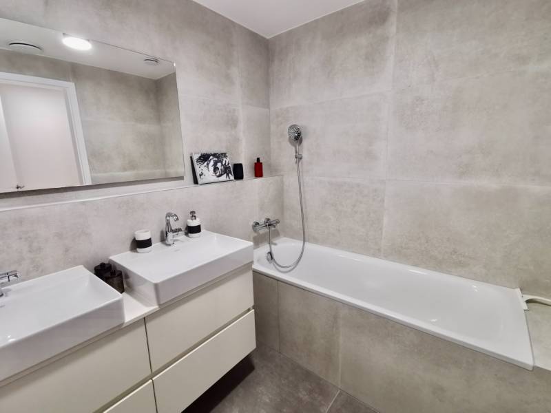 A bathroom in a 3-room apartment with two sinks, a bathtub, and a large mirror.