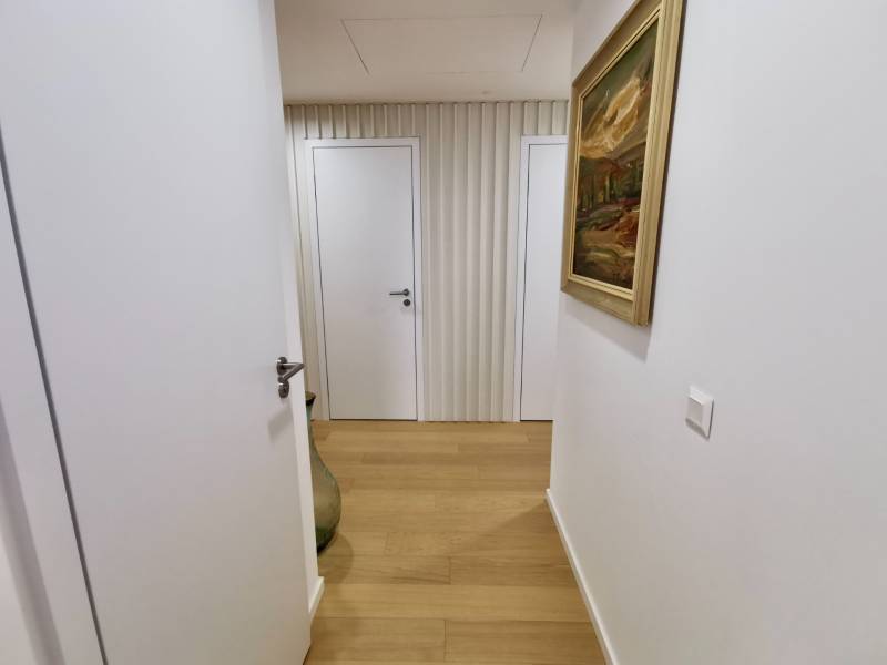 A hallway in a 3-room apartment with a wooden decor floor, a painting on the wall, and white doors.