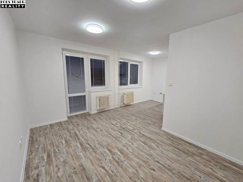 An office with white walls and a wooden decor floor, with a window and a radiator.