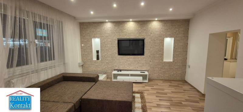 Living room in a family house with a wooden decor floor and a television on a stone wall.