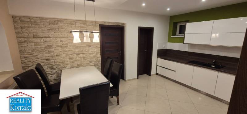 Dining room in a family house with a white table, dark chairs, and stone cladding.